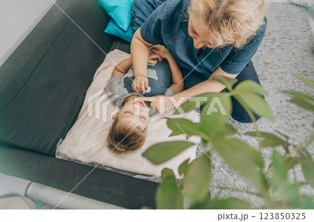 smiling boy lying on blanket during a therapy session with a female specialist in a cozy room, concept of relaxation, childhood therapy, and healthcare 123850325