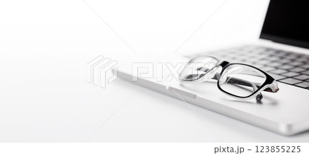 Closeup of an office table featuring a sleek laptop and reading glasses on a clean white surface 123855225