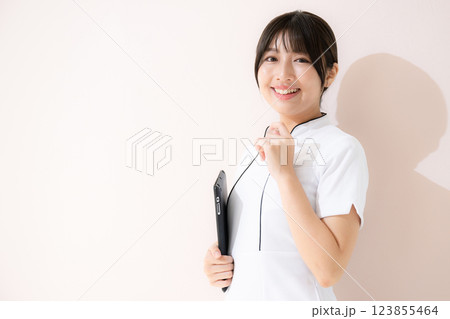 タブレットを持つエステや美容ナースなど受付やカウンセリングのポーズの正面 ピンク背景 タブレットを持つエステや美容ナースなど受付やカウンセリングのポーズの正面 ピンク背景 123855464