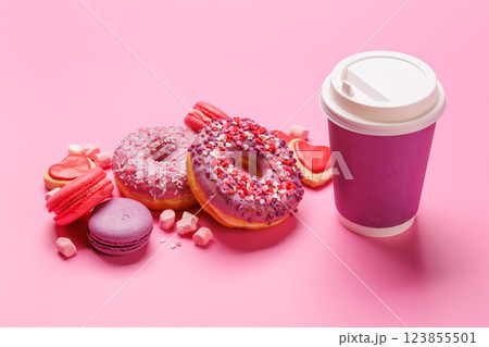 A cheerful display of colorful macarons, donuts, and a paper coffee cup on a pastel pink background 123855501