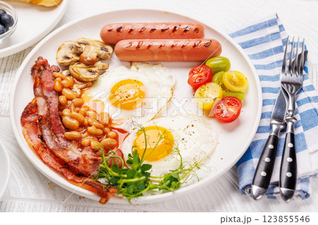 A classic breakfast plate featuring sunny-side-up eggs, crispy bacon, sausages, and fresh tomatoes 123855546