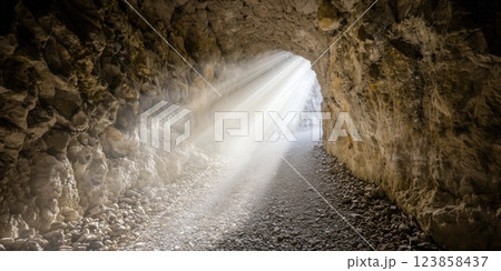 Light beams entering dark stone cave tunnel inspiring hope and faith 123858437