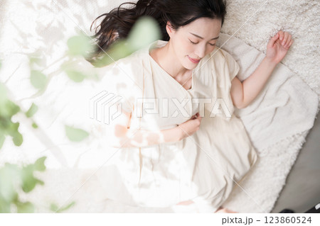 仰向けで目を閉じる美しい大人の女性　お昼寝や睡眠イメージ　緑の前ボケあり	 123860524