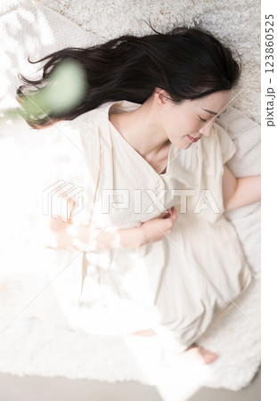 仰向けで目を閉じる美しい大人の女性　お昼寝や睡眠イメージ　緑の前ボケあり	 123860525