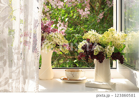 Still life with blooming lilac flowers in a vase and a cup of tea on a sunny window, abstract floral arrangement, Home interior with decor elements, floral birthday card, wedding, 123860581