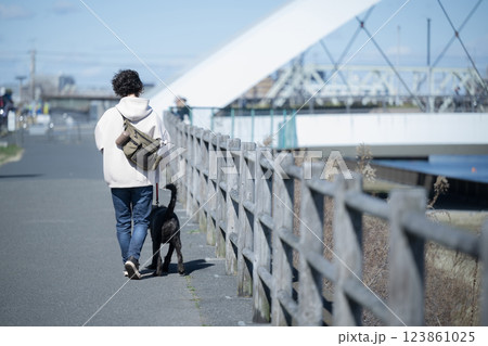 橋のある河川敷で大型犬の散歩を楽しむ男性 顔無しの後ろ姿 橋のある河川敷で大型犬の散歩を楽しむ男性 顔無しの後ろ姿 123861025