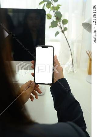 Over shoulder view of woman holding smartphone with blank screen, sitting at a modern workspace Over shoulder view of woman holding smartphone with blank screen, sitting at a modern workspace 123861106