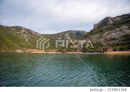 Trees and reeds on River Crnojevica, place near Lake Skadar in Montenegro surrounded by mountain peaks in winter time Trees and reeds on River Crnojevica, place near Lake Skadar in Montenegro surrounded by mountain peaks in winter time 123861168