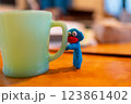 コーヒーカップに掴まる粘土で作った青いキャラ 123861402