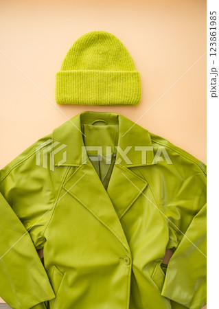 Flat lay of green faux leather coat , cashmere hat made from recycled materials on beige background. Flat lay of green faux leather coat , cashmere hat made from recycled materials on beige background. 123861985