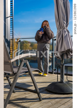 Defocus woman on a sunny terrace in autumn Prague, holding coffee and smartphone in a faux fur coat 123861999
