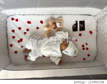 Newborn Baby Sleeping in Crib with Hearts and Teddy Bear 123862186