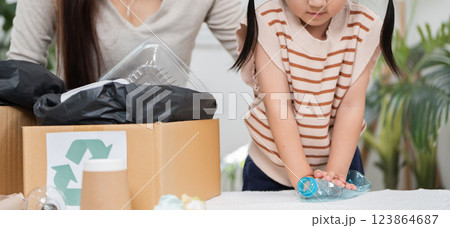 Waste Reduction and Family Engagement. A mother guiding her daughter as they sort plastic waste for recycling in their living room. Waste Reduction and Family Engagement. A mother guiding her daughter as they sort plastic waste for recycling in their living room. 123864687