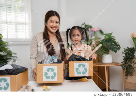 Eco-Friendly Practices and Family Togetherness. A mother smiling with her daughter while sorting recyclable materials into labeled boxes. 123864695