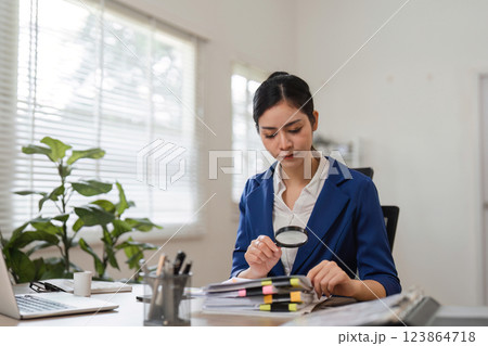 Detailed financial review. Businesswoman examining documents with a magnifying glass in a modern office. 123864718
