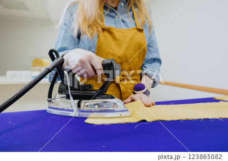 woman strokes a piece of cloth of lady in yellow apron, glasses. female fashion designer woman strokes a piece of cloth of lady in yellow apron, glasses. female fashion designer 123865082