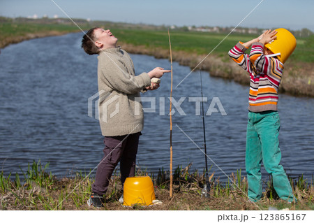 Funny photo of fishermen. Two boys are fishing and having fun. One of them put a bucket on his head. Funny photo of fishermen. Two boys are fishing and having fun. One of them put a bucket on his head. 123865167