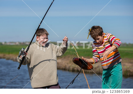 Funny fishing. Two of the boy's friends hooked an old shoe with a fishing rod and are laughing. 123865169