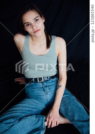 Beautiful slim woman in jeans sitting on black background 123865540