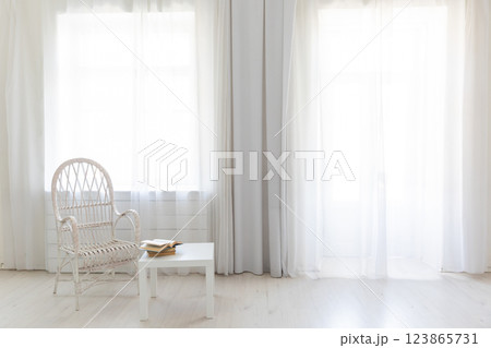 Chair and table with books in the interior of an empty white room with a window 123865731