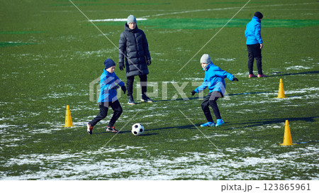 Group of young athletes engaged in active football drill, coach directing movement, cold outdoor practice. Passion and hard work. Group of young athletes engaged in active football drill, coach directing movement, cold outdoor practice. Passion and hard work. 123865961