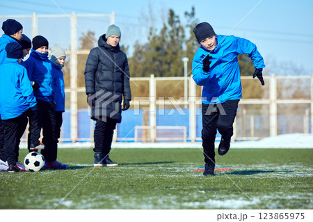 Building Coordination. Junior soccer player training dribbling speed and agility in snowy outdoor stadium. Motivation and progress. 123865975