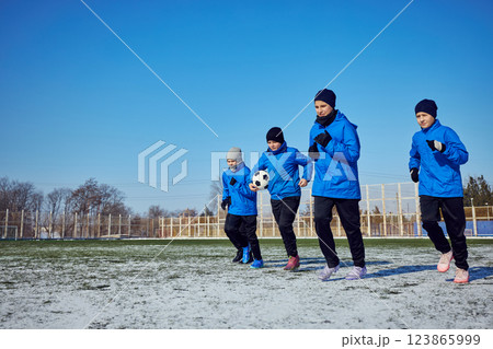 Strength in Unity. Young football players in matching uniforms running on frozen pitch, pushing through winter conditions. Strength in Unity. Young football players in matching uniforms running on frozen pitch, pushing through winter conditions. 123865999