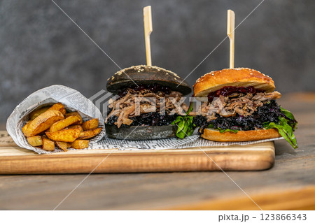 Burger with pulled meat in a dark and light bun with fresh vegetables and french fries on a wooden board Burger with pulled meat in a dark and light bun with fresh vegetables and french fries on a wooden board 123866343