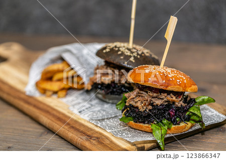 Burger with pulled meat in a dark and light bun with fresh vegetables and french fries on a wooden board 123866347