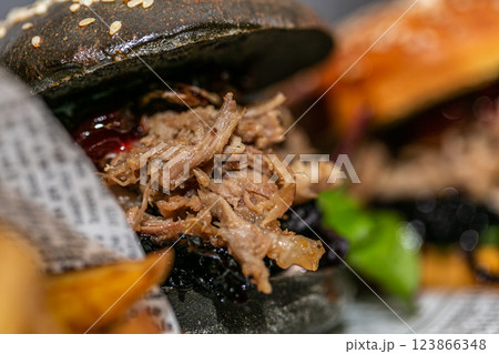 Burger with pulled meat in a dark and light bun with fresh vegetables and french fries on a wooden board 123866348