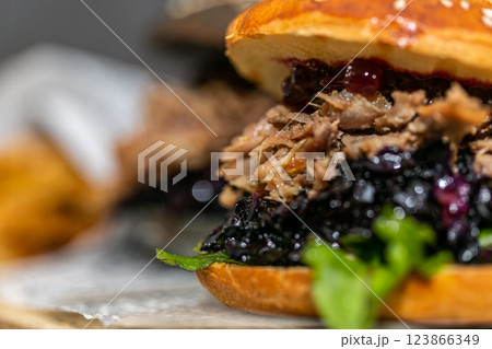 Burger with pulled meat in a dark and light bun with fresh vegetables and french fries on a wooden board 123866349