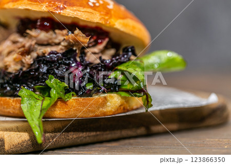 Burger with pulled meat in a dark and light bun with fresh vegetables and french fries on a wooden board 123866350