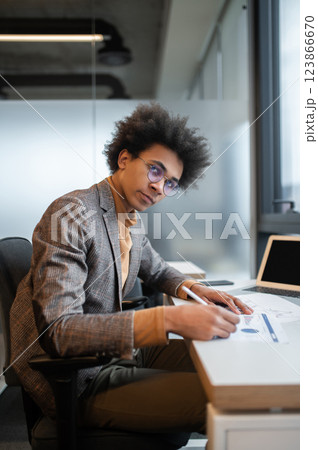 Dark-skinned businessman working on the project and looking serious Dark-skinned businessman working on the project and looking serious 123866670