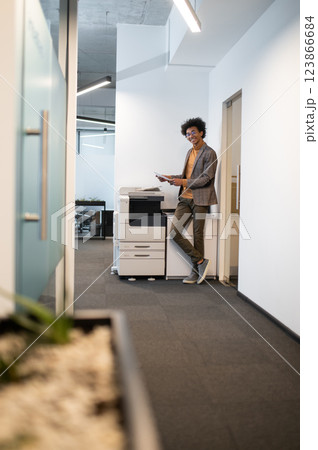 Curly-haired young businessman standing near xerox and making documents copies Curly-haired young businessman standing near xerox and making documents copies 123866684