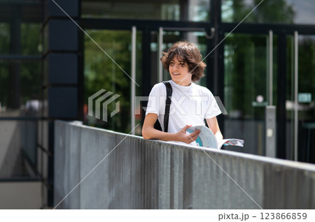 Dark-haired teenager standing near school building with a book in hands 123866859