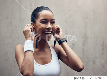 Music, fitness and exercise with a sports woman streaming audio during training or a workout on a gray background. Health, cardio and training with a female runner listening on earphones during a run 123867856