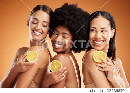 Skincare, diversity and women, beauty and lemon for health, wellness and nutrition on orange studio background. Friends, smile and happy models with fruit for vitamin c, healthy or glowing skin. 123868304