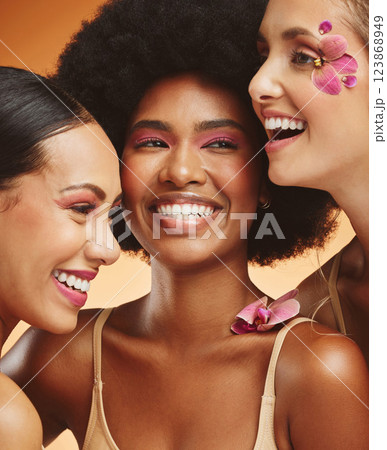 Women, beauty and flowers, makeup and diversity of models on orange studio background. Skincare, face and happy, young and elegant female group posing together with cosmetics, orchids or pink plants. 123868949