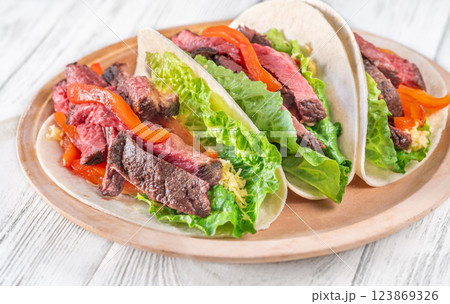 Three carne asada tacos filled with steak, grilled peppers, lettuce, and cheese Three carne asada tacos filled with steak, grilled peppers, lettuce, and cheese 123869326