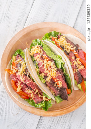 Three carne asada tacos filled with steak, grilled peppers, lettuce, and cheese 123869329