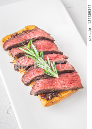 Grilled ciabatta sandwich with melted cheese, juicy steak, caramelized onions, and rosemary 123869345