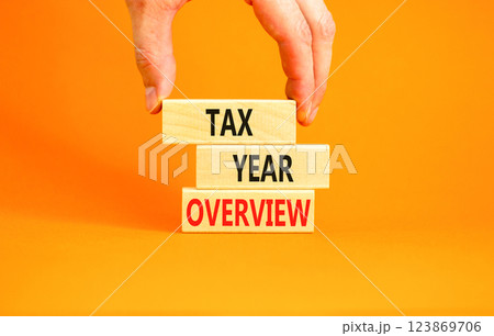 Tax year overview symbol. Concept words Tax year overview on beautiful wooden blocks. Beautiful orange background. Businessman hand. Business tax year overview concept. Copy space. Tax year overview symbol. Concept words Tax year overview on beautiful wooden blocks. Beautiful orange background. Businessman hand. Business tax year overview concept. Copy space. 123869706