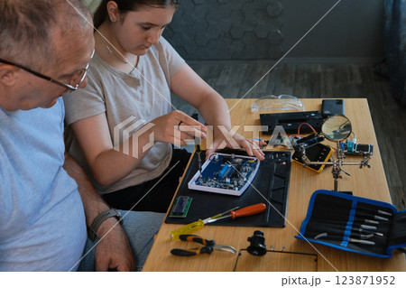 Grandfather and granddaughter work together on an electronics project 123871952