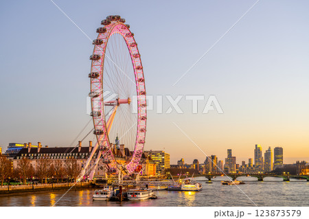 The London Eye stands tall on the South Bank of the River Thames, illuminated in pink hues as evening falls. Boats glide on the water, framed by a vibrant city skyline. The London Eye stands tall on the South Bank of the River Thames, illuminated in pink hues as evening falls. Boats glide on the water, framed by a vibrant city skyline. 123873579
