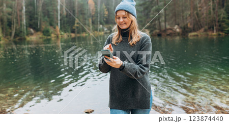 Phone Communication. Check social networks. 30s Traveler woman in hat standing with phone near the majestic lake. Travel, adventure. Concept of an active lifestyle. 123874440