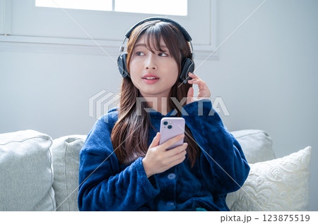 冬のリビングでスマホを持ってヘッドホンで音楽を聴く女性 123875519
