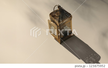 Golden metal ornamental Moroccan lantern on beige table in sunlight, long shadows. Blurred background, top view. Festive banner still life for Muslim holiday Ramadan Kareem. Eid mubarak celebration. 123875952