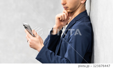 スマートフォンを見て考える男性ビジネスマン スマートフォンを見て考える男性ビジネスマン 123876447