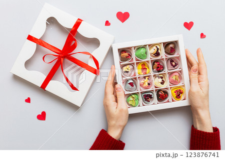 Female hands with delicious candies in box on color background Female hands with delicious candies in box on color background 123876741