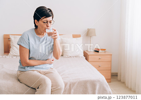 Mature caucasian woman drinking water in bedroom Mature caucasian woman drinking water in bedroom 123877011